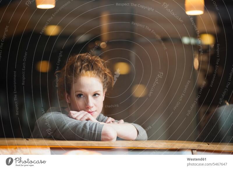 Nachdenkliche junge Frau, die sich auf einen Tisch lehnt und durch ein Glasfenster im Café gesehen wird Farbaufnahme Farbe Farbfoto Farbphoto Außenaufnahme