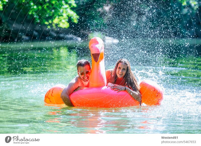 Paar schwimmt auf Wasser auf einem aufblasbaren Flamingo auf dem Wasser treiben planschen plantschen spritzen Sommer Sommerzeit sommerlich lachen baden Pärchen