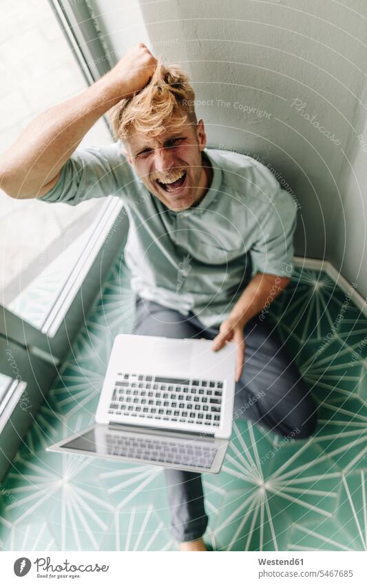 Junger Mann sitzt auf dem Boden, hält Laptop, schreit in Verzweiflung Unternehmer Arbeitgeber schreien rufen rufend Schrei schreiend Wut wütend Zorn Rage zornig