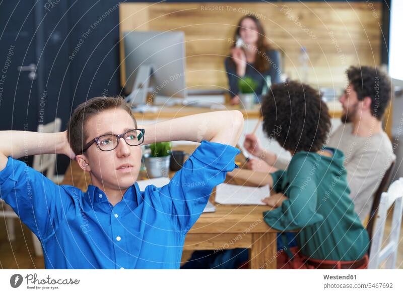 Junger Mann denkt im Büro mit Kollegen im Hintergrund denken nachdenken Männer männlich Office Büros Coworker Erwachsener erwachsen Mensch Menschen Leute People
