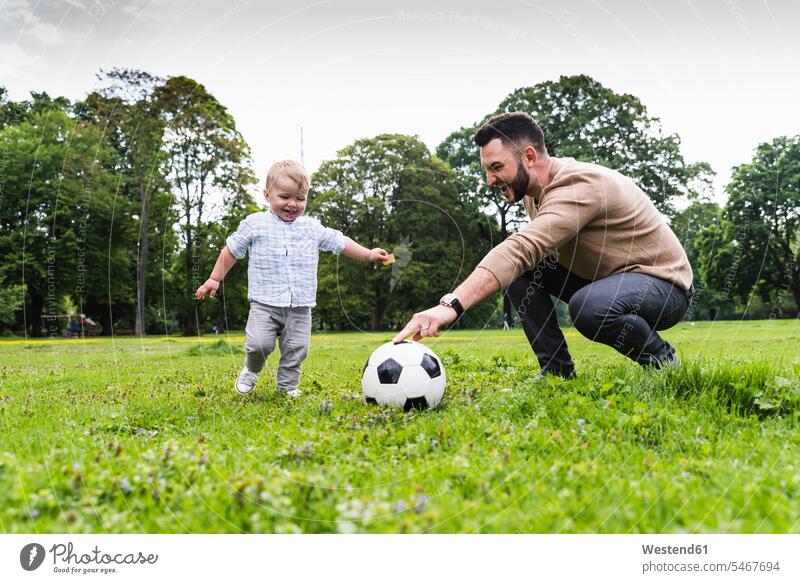 Glücklicher Vater spielt mit seinem Sohn in einem Park Fussball spielen aktiv glücklich glücklich sein glücklichsein Parkanlagen Parks Fußball Papas Väter Vati