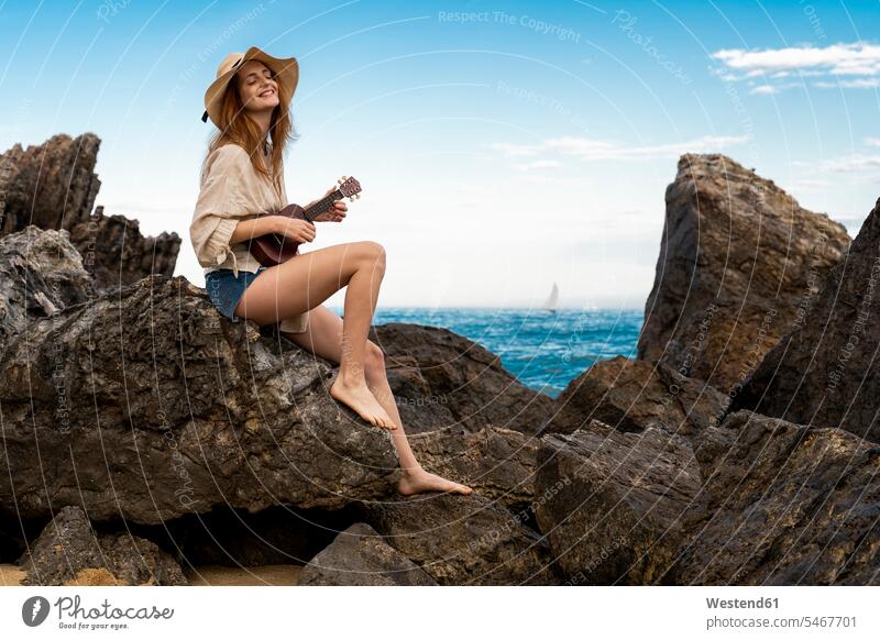 Glückliche junge Frau sitzt auf einem Felsen und spielt Ukulele Spanien Ufer musizieren Musik machen Unbeschwert Sorglos Schönheit Beauty Hochgefühl Heiterkeit