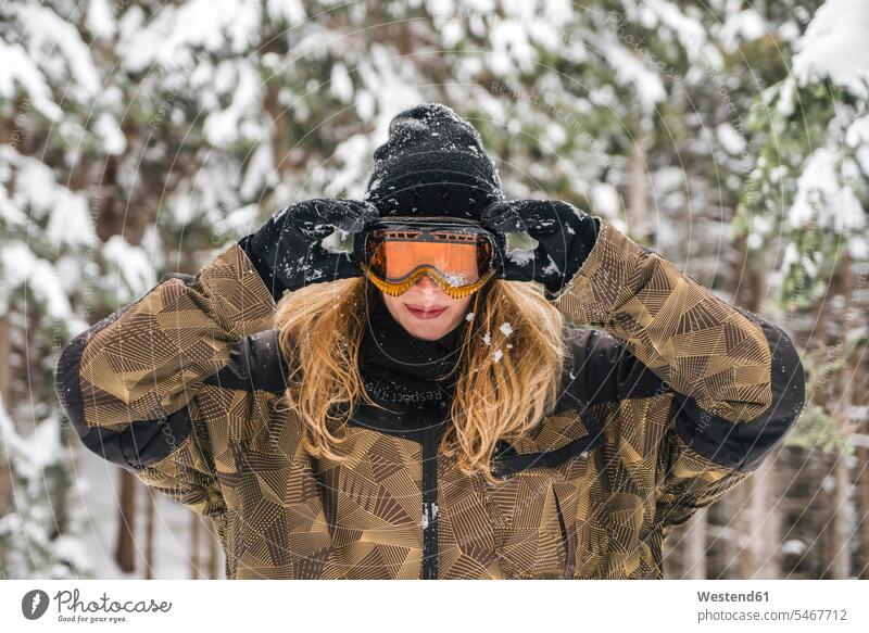 Junge Frau setzt Skibrille im Winterwald auf Wald Forst Wälder aufsetzen winterlich Winterzeit Skibrillen Schibrillen weiblich Frauen Skifahren Skisport