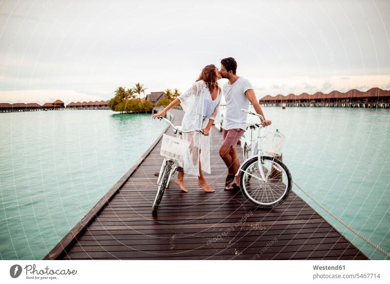 Paar mit Fahrrädern küsst sich auf einem Steg im Meer, Insel Maguhdhuvaa, Gaafu-Dhaalu-Atoll, Malediven Raeder Räder Bike Bikes Rad Kuss Küsse Jahreszeiten