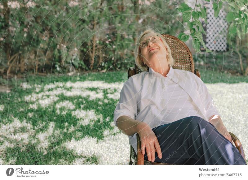 Nachdenkliche ältere Frau schaut auf, während sie sich auf einem Stuhl im Hof entspannt Farbaufnahme Farbe Farbfoto Farbphoto Spanien Freizeitbeschäftigung Muße