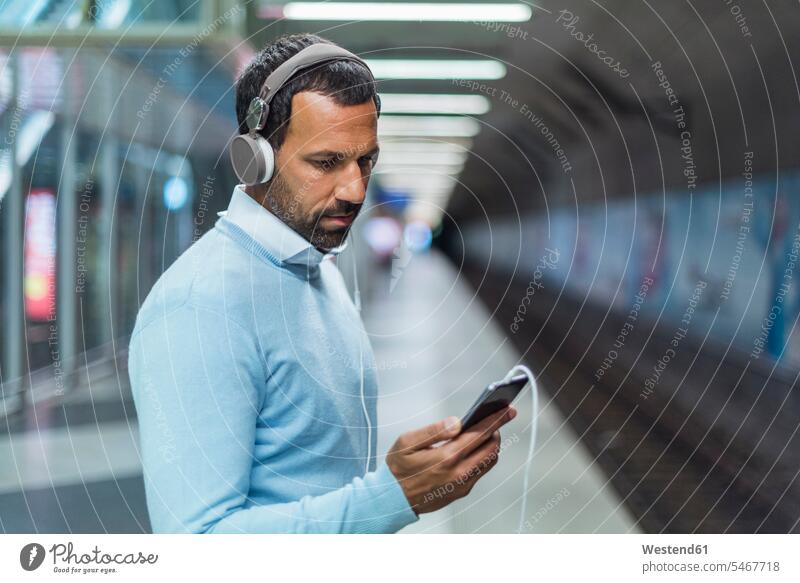 Geschäftsmann benutzt Smartphone an der U-Bahn-Station telefonieren anrufen Anruf telephonieren Ohrhörer Portrait Porträts Portraits hören hoeren Musik