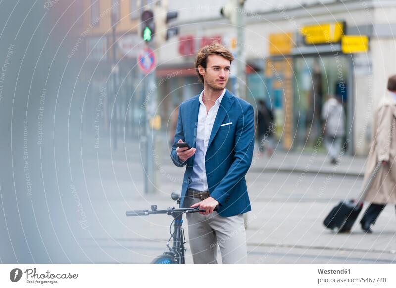 Porträt eines jungen Geschäftsmannes mit Fahrrad und Smartphone, der in der Stadt wartet geschäftlich Geschäftsleben Geschäftswelt Geschäftsperson