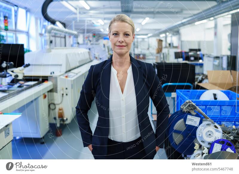 Selbstbewusst lächelnde Geschäftsfrau steht mit den Händen in den Taschen in einer beleuchteten Fabrik Farbaufnahme Farbe Farbfoto Farbphoto Innenaufnahme