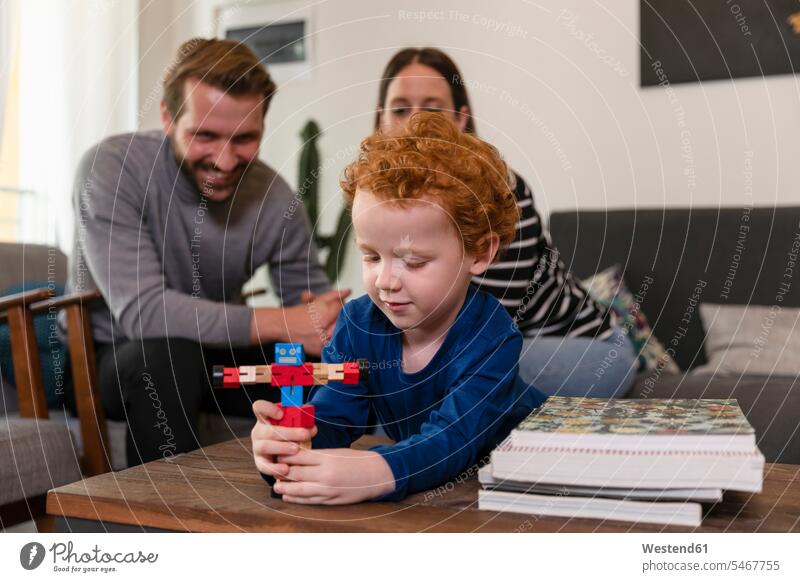 Eltern sehen süßen Sohn beim Spielen mit Spielzeugroboter auf dem Tisch im Wohnzimmer Farbaufnahme Farbe Farbfoto Farbphoto Freizeitbeschäftigung Muße Zeit