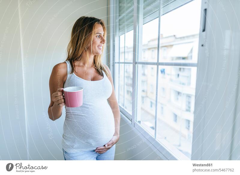 Schwangere Frau schaut aus dem Fenster und hält einen Becher schwanger schwangere Frau halten weiblich Frauen Erwachsener erwachsen Mensch Menschen Leute People