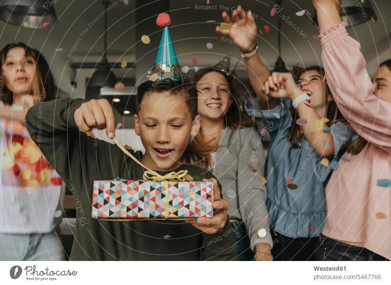 Neugieriges Geburtstagskind öffnet Geschenk, während Freunde im Hintergrund tanzen Farbaufnahme Farbe Farbfoto Farbphoto Deutschland Innenaufnahme