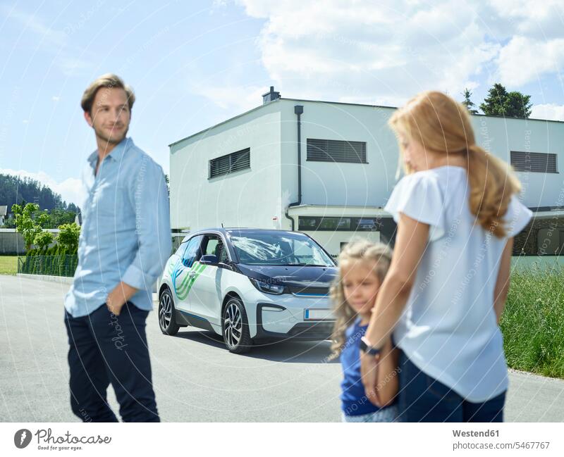 Familie mit Elektroauto vor dem Haus Elektromobil Elektromobile Elektroautos Familien Auto Wagen PKWs Automobil Autos Häuser Haeuser Elektrofahrzeug