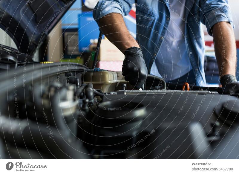 Mann in Hemd und Handschuhen arbeitet in einer Autowerkstatt und repariert einen Automotor Job Berufe Berufstätigkeit Beschäftigung Jobs Hemden KFZ