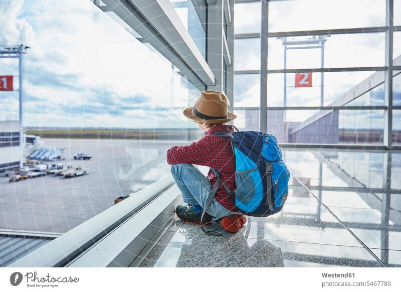 Junge sitzt hinter einer Fensterscheibe am Flughafen und schaut auf das Flugfeld Flughaefen Airport Airports Flughäfen Buben Knabe Jungen Knaben männlich
