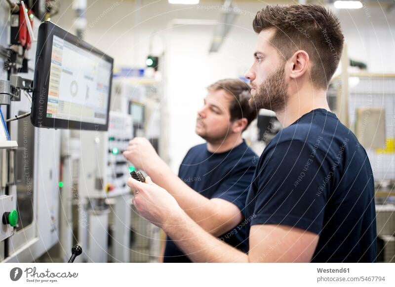 Zwei Männer arbeiten in einer modernen Fabrik und bedienen gemeinsam eine Maschine Arbeitskollege Arbeitskollegen Kollege Job Berufe Berufstätigkeit