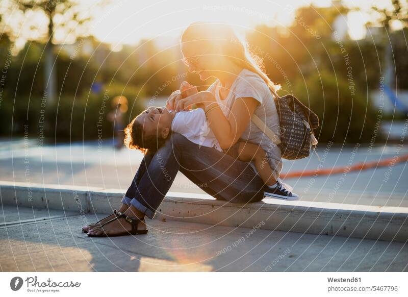 Glückliche Mutter spielt mit ihrem kleinen Sohn auf einem Platz bei Sonnenuntergang Söhne Plätze Plaetze glücklich glücklich sein glücklichsein Mami Mutti