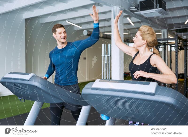 Ein glücklicher Mann und eine glückliche Frau, die während des Laufbandtrainings im Fitnessstudio das High Five machen weiblich Frauen Männer männlich laufen