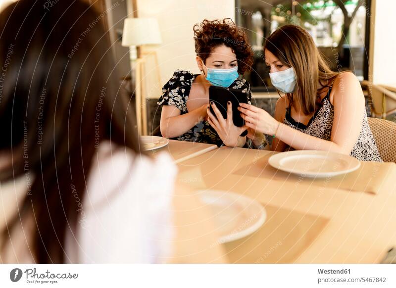 Frauen, die Masken tragen, während sie mit einem digitalen Tablet am Tisch im Restaurant sitzen Farbaufnahme Farbe Farbfoto Farbphoto Spanien Innenaufnahme