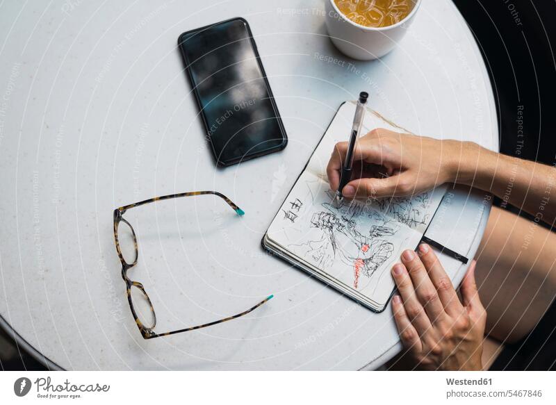 Hände einer Frau, die in einem Notizbuch, mit Brille, Tee und Smartphone auf dem Tisch skizziert Skizze Entwurf Entwürfe Entwuerfe Skizzen Tees schreiben