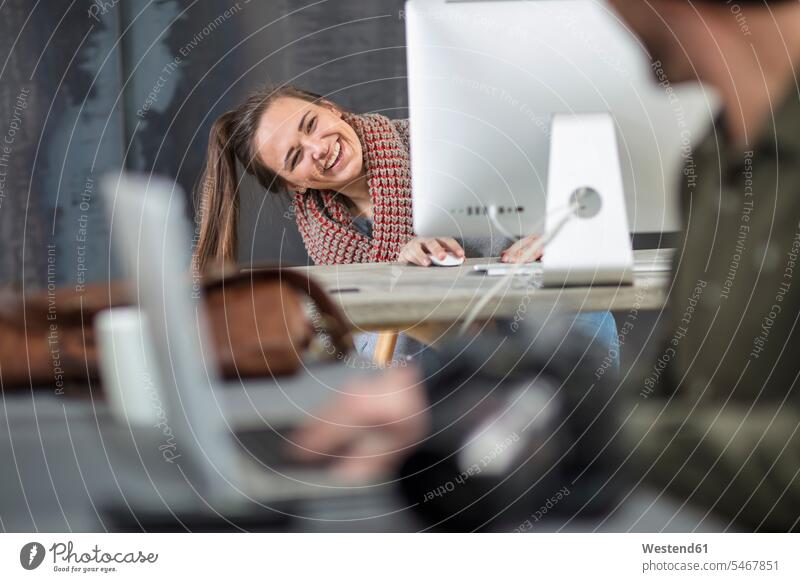 Glückliche junge Frau, die im Büro auf den Computerbildschirm schaut Computermonitor glücklich glücklich sein glücklichsein gucken blicken schauen lugen