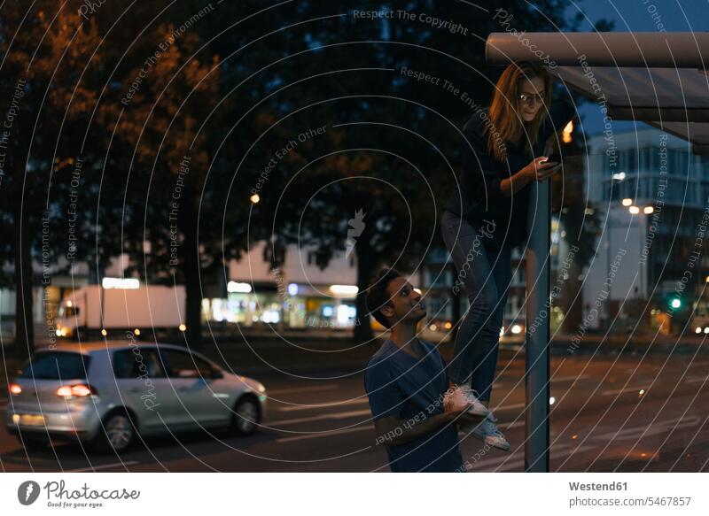 Junger Mann gibt Freundin mit Handy ein Bein-up in der Stadt in der Nacht Räuberleiter Raeuberleiter Mobiltelefon Handies Handys Mobiltelefone nachts Paar