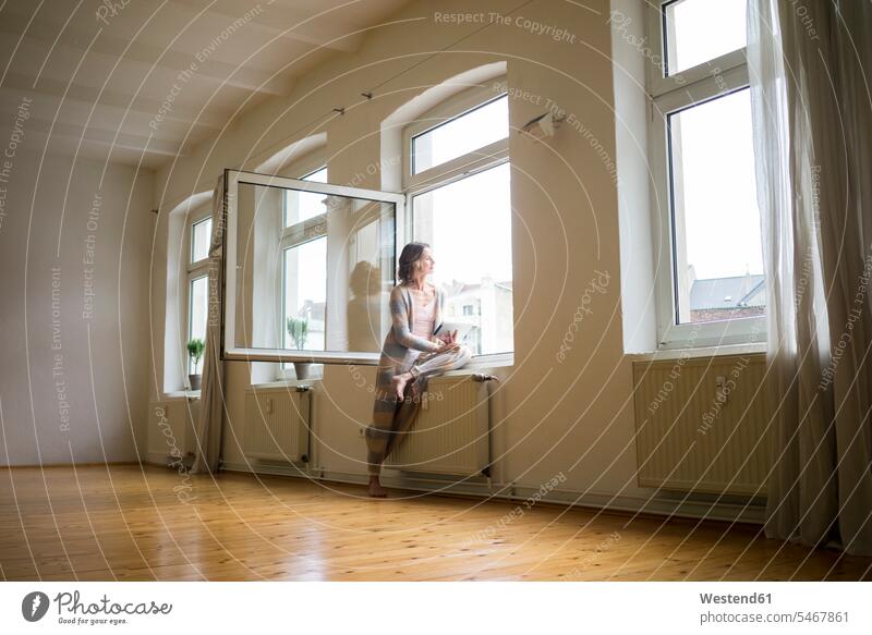 Reife Frau im leeren Raum hält Tablette und schaut aus dem Fenster Tag am Tag Tageslichtaufnahme tagsueber Tagesaufnahmen Tageslichtaufnahmen tagsüber weiblich
