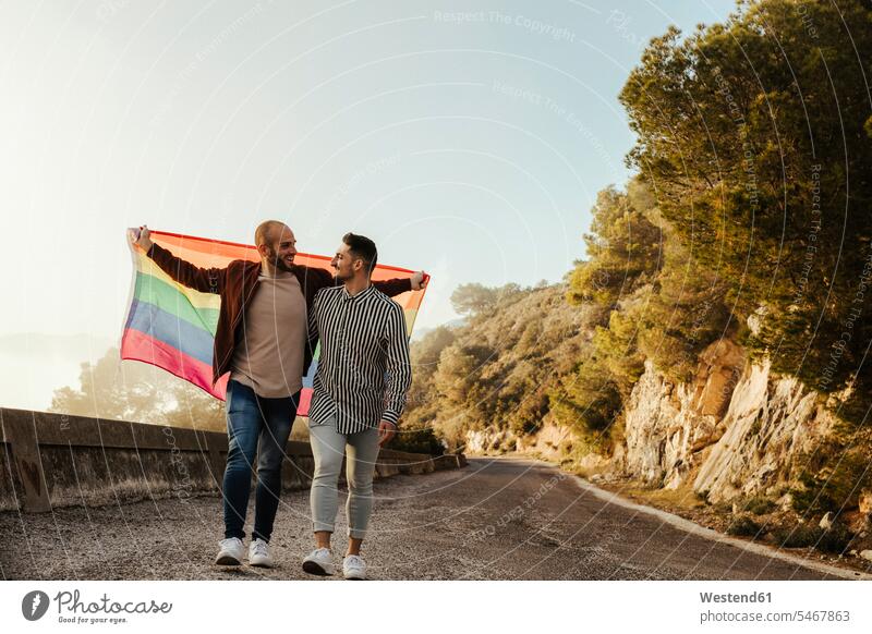 Homosexuelles Paar mit Homosexuell Stolz Flagge zu Fuß auf einer Straße in den Bergen Fahnen Flaggen gehend geht reden freuen Glück glücklich sein glücklichsein