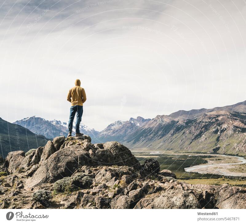 Älterer Mann mit Kapuze schaut Berge gegen den Himmel an, während er auf Fels steht, Patagonien, Argentinien Südamerika Patagonische Anden Farbaufnahme Farbe