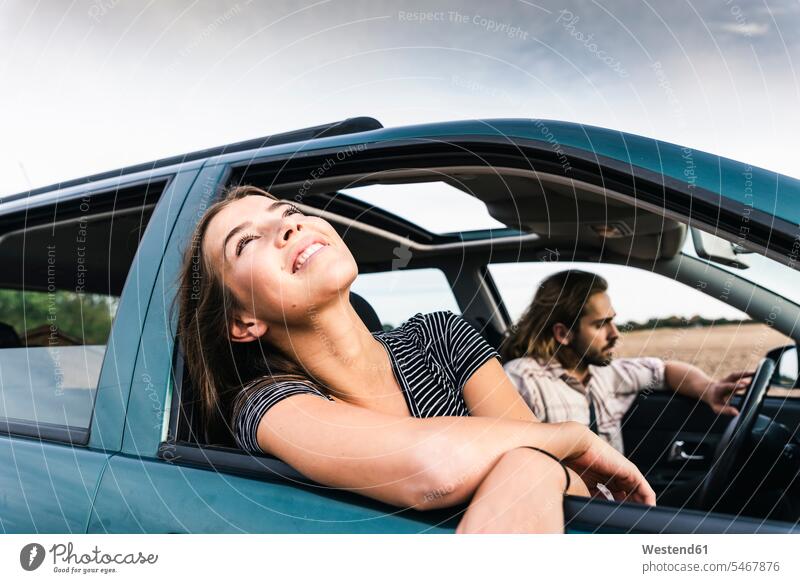 Lächelnde junge Frau lehnt sich aus dem Autofenster Fenster Wagen PKWs Automobil Autos weiblich Frauen lächeln Kraftfahrzeug Verkehrsmittel KFZ Erwachsener