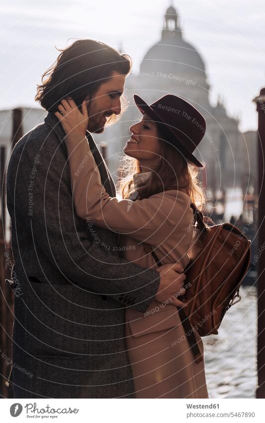 Liebenswertes junges Paar am Wasser in Venedig, Italien Rucksäcke Hüte Jacken Kuss Küsse Arm umlegen Umarmung Umarmungen freuen geniessen Genuss Glück