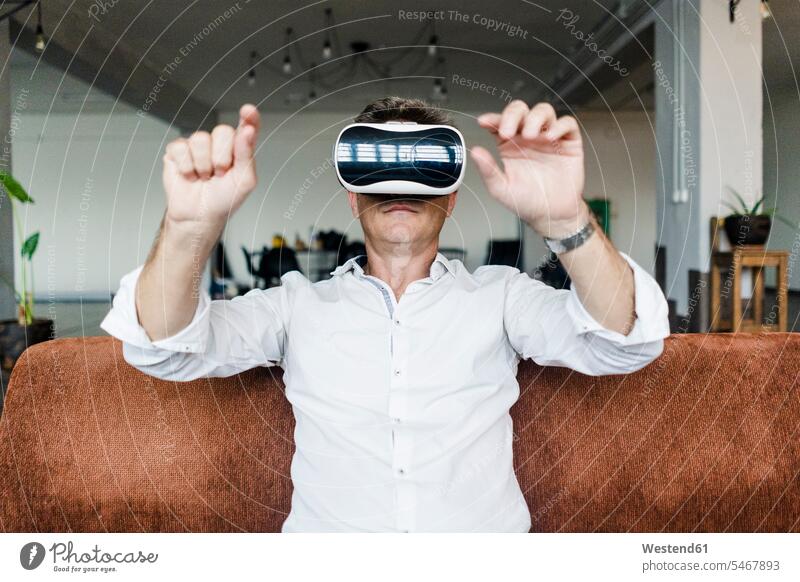 Reifer Mann mit VR-Brille sitzt auf Couch in einem Loft Lofts sitzen sitzend Virtuelle Realität Virtuelle Realitaet Brillen Männer männlich Sofa Couches Liege