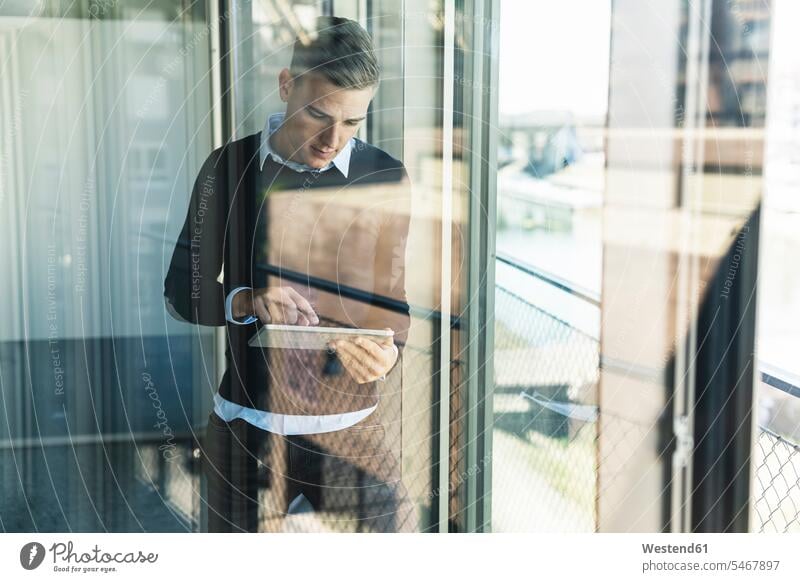 Männlicher Fachmann arbeitet über ein digitales Tablett, während er im Büro steht und durch ein Fenster gesehen wird Farbaufnahme Farbe Farbfoto Farbphoto