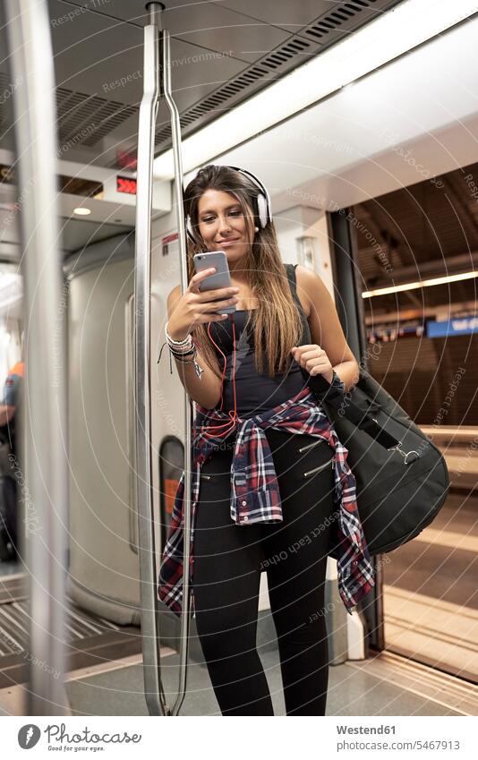 Porträt einer lächelnden Frau mit Gitarrenrucksack und Kopfhörern, die in der U-Bahn auf ihr Handy schaut Rucksack Rucksäcke Smartphone iPhone Smartphones