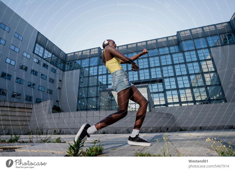 Junge Frau tanzt auf Fußweg gegen Gebäude in der Stadt Farbaufnahme Farbe Farbfoto Farbphoto Freizeitbeschäftigung Muße Zeit Zeit haben Freizeitkleidung