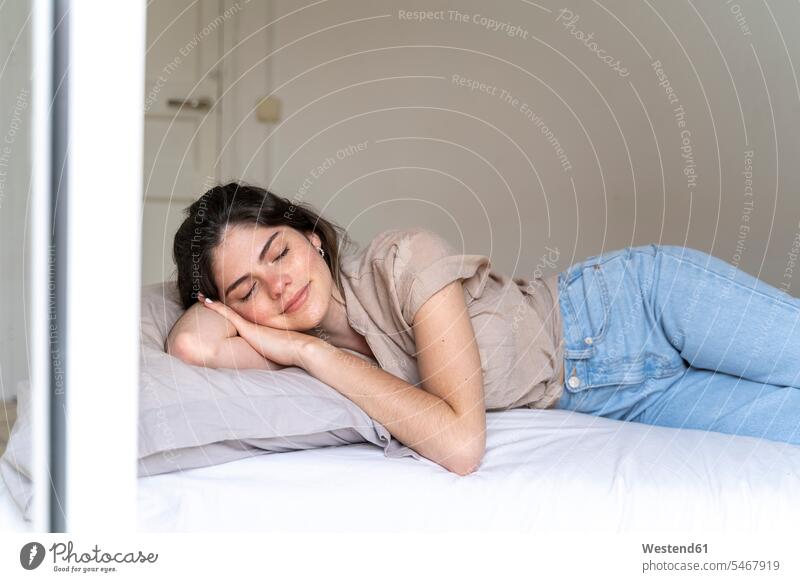 Lächelnde junge Frau, die mit geschlossenen Augen auf dem Bett liegt Hemden Hosen Jeanshose Betten entspannen relaxen schlafend entspanntheit relaxt freuen