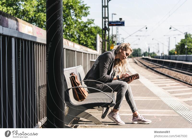 Junge Frau sitzt am Bahnhof und benutzt ein digitales Tablett Bahnhöfe Bahnhoefe junge Frau junge Frauen Tablet Computer Tablet-PC Tablet PC iPad