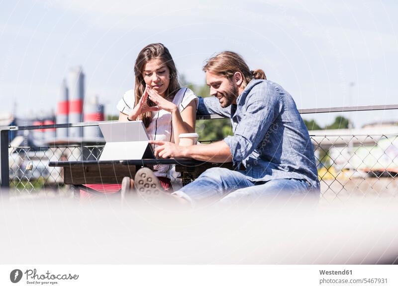Junges Paar mit Tablet in einem Biergarten Hochschueler Hochschüler Studenten Studierende Studierender Tische Holztische sitzend sitzt sommerlich Sommerzeit