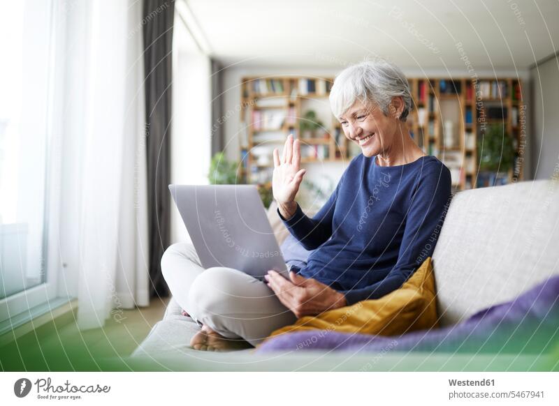 Ältere Frau macht High Five bei Videoanrufen, während sie zu Hause einen Laptop benutzt Farbaufnahme Farbe Farbfoto Farbphoto Innenaufnahme Innenaufnahmen innen