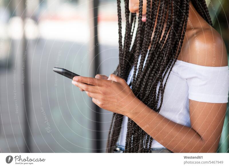 Junge Frau benutzt Mobiltelefon, während sie sich in der Stadt an eine Glaswand lehnt Farbaufnahme Farbe Farbfoto Farbphoto Außenaufnahme außen draußen
