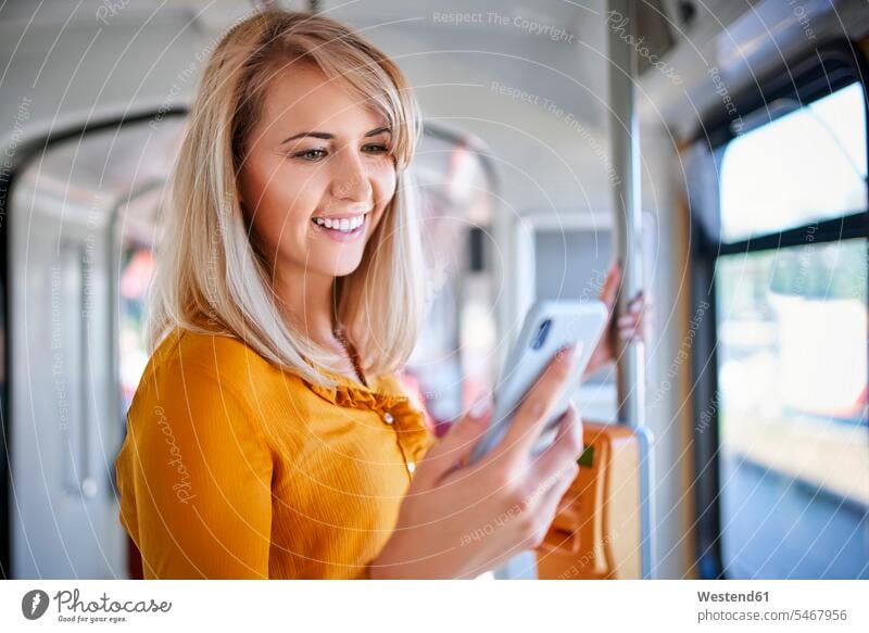 Lächelnde junge Frau mit Smartphone in der Straßenbahn Leute Menschen People Person Personen Europäisch Kaukasier kaukasisch 1 Ein ein Mensch eine