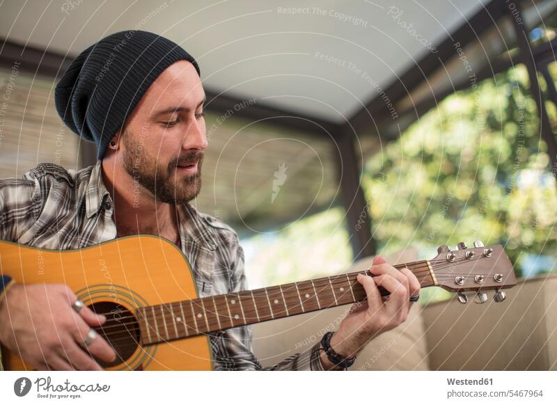 Junger Mann sitzt zu Hause auf dem Sofa und spielt Gitarre sitzen sitzend Musik Gitarren Couches Liege Sofas musizieren Musik machen Zuhause daheim Männer
