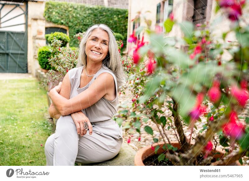 Glückliche Frau mit langen grauen Haaren sitzt im Garten glücklich glücklich sein glücklichsein Gärten Gaerten sitzen sitzend weiblich Frauen Erwachsener
