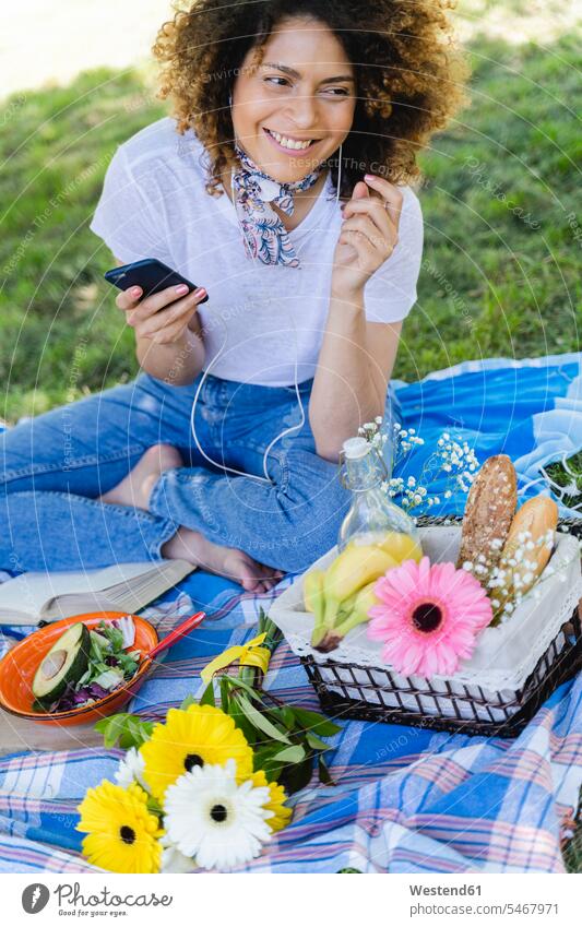 Entspannte Frau mit Handy und Kopfhörern beim Picknick im Park Leute Menschen People Person Personen 1 Ein ein Mensch eine nur eine Person single erwachsen