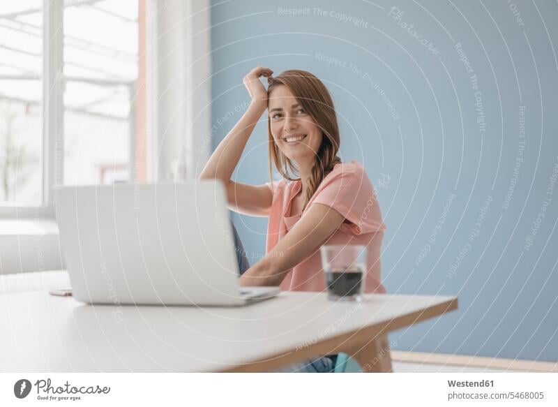 Frau zu Hause sitzt am Schreibtisch mit Laptop sitzen sitzend benutzen benützen Zuhause arbeiten von zuhause arbeiten arbeiten von zuhause aus weiblich Frauen