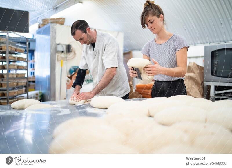 Mann und Frau bereiten in einer Bäckerei Brotlaibe zu Arbeitskollege Arbeitskollegen Kollege Job Berufe Berufstätigkeit Beschäftigung Jobs Gewerbe Handwerker