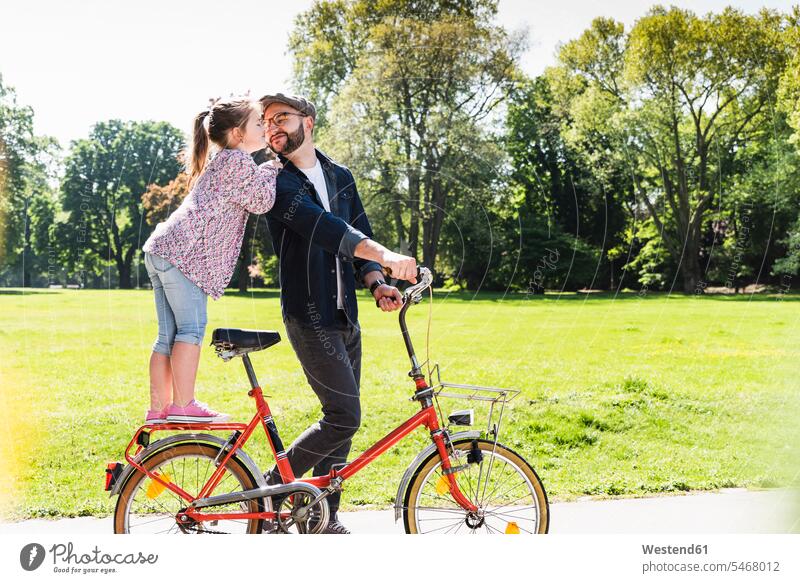 Tochter küsst Vater mit Fahrrad in einem Park Töchter küssen Küsse Kuss Bikes Fahrräder Räder Rad Papas Väter Vati Vatis Papis aktiv Parkanlagen Parks Kind