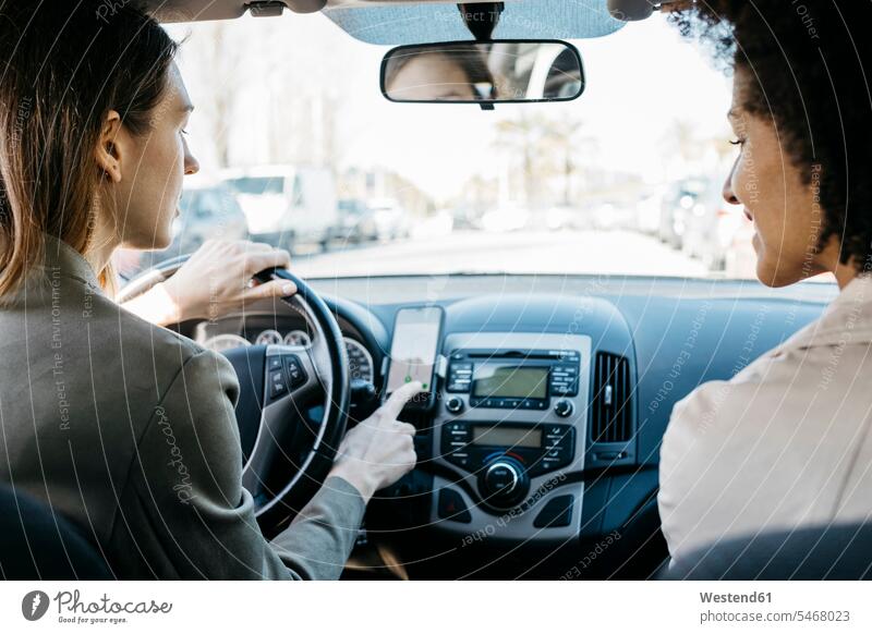 Zwei Frauen, die in einem Auto durch die Stadt fahren und eine telefonische Navigations-App verwenden Freundinnen Anwendung application Apps weiblich staedtisch