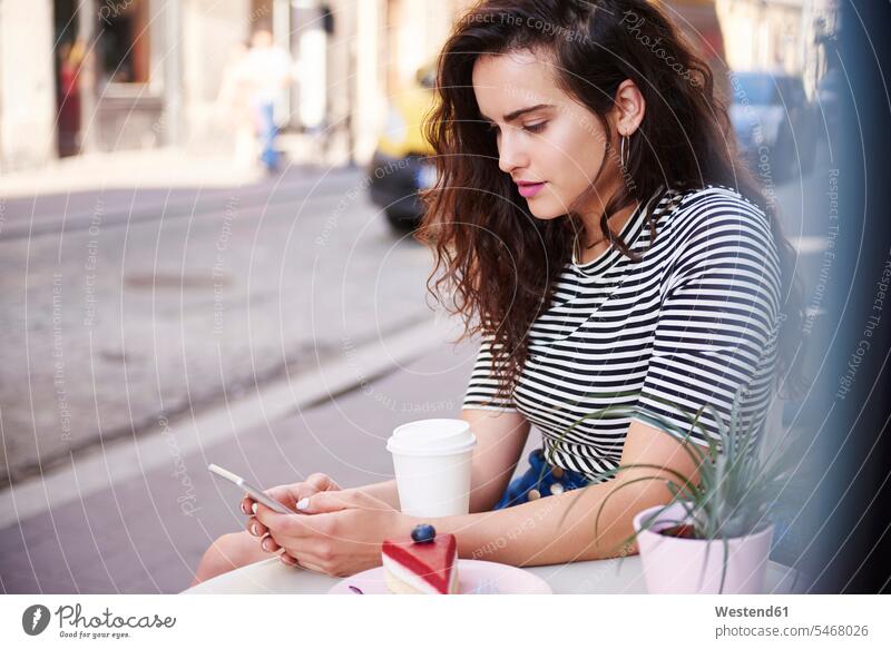 Junge Frau benutzt Handy im Straßencafé in der Stadt Mobiltelefon Handies Handys Mobiltelefone staedtisch städtisch Cafe Kaffeehaus Bistro Cafes Café Cafés