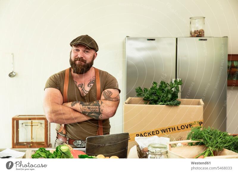 Besitzer eines Lieferservices für Bio-Gemüse, steht stolz in seiner Küche Karton Pappkartons Kartons vegan vegane Gemuese einpacken einwickeln Karotte Karotten