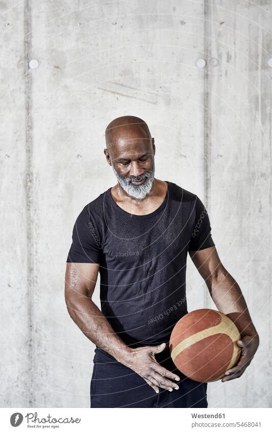 Älterer Mann hält Basketball an Betonwand Männer männlich halten Betonwände Betonwaende Sport Erwachsener erwachsen Mensch Menschen Leute People Personen Wand
